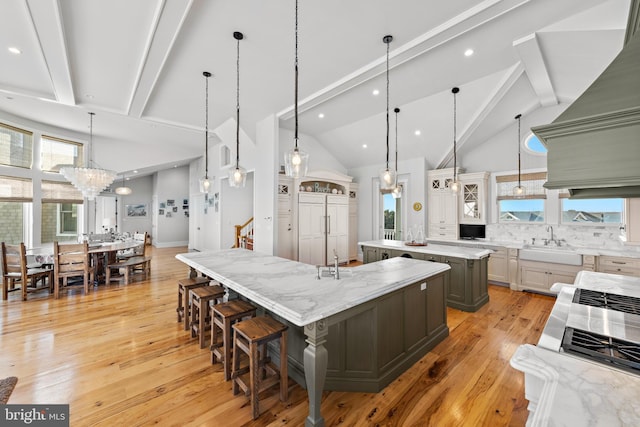 kitchen featuring light stone countertops, a large island, sink, hanging light fixtures, and light hardwood / wood-style floors