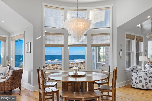 dining room with light hardwood / wood-style floors, a water view, a towering ceiling, and an inviting chandelier