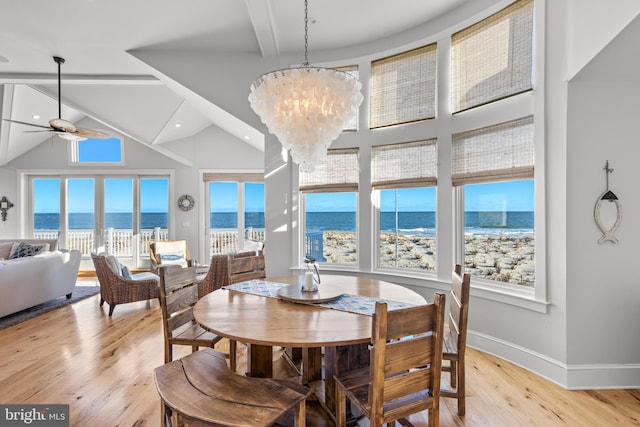 dining space with high vaulted ceiling, ceiling fan with notable chandelier, a water view, a view of the beach, and light hardwood / wood-style floors