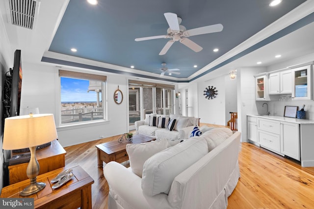 living room with light hardwood / wood-style floors, a raised ceiling, ceiling fan, and sink