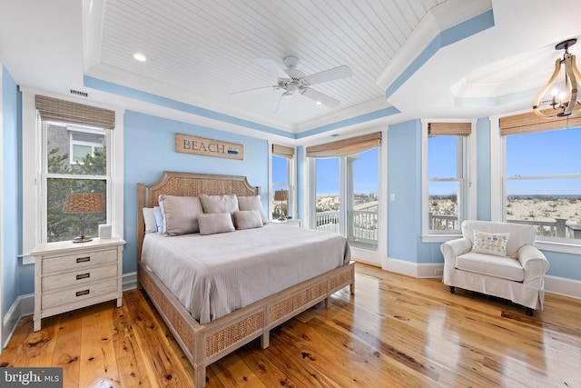 bedroom with a tray ceiling, multiple windows, light hardwood / wood-style floors, and ceiling fan