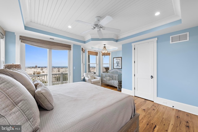 bedroom with ceiling fan with notable chandelier, a tray ceiling, and light hardwood / wood-style floors