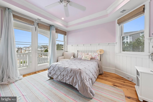 bedroom featuring access to exterior, light wood-type flooring, a tray ceiling, and ceiling fan