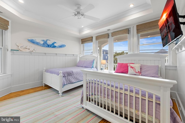 bedroom featuring a tray ceiling, light hardwood / wood-style flooring, ceiling fan, and crown molding