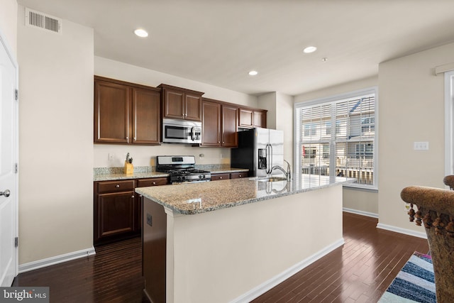 kitchen with a center island with sink, dark hardwood / wood-style flooring, light stone counters, and appliances with stainless steel finishes