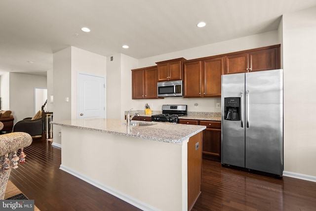 kitchen with light stone counters, stainless steel appliances, a kitchen island with sink, sink, and dark hardwood / wood-style floors