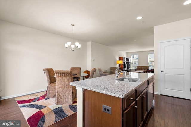 kitchen featuring light stone counters, dark wood-type flooring, sink, pendant lighting, and an island with sink