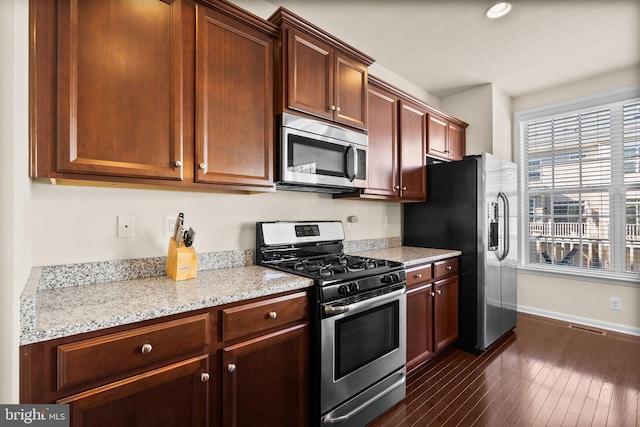 kitchen with stainless steel appliances, light stone counters, and dark wood-type flooring