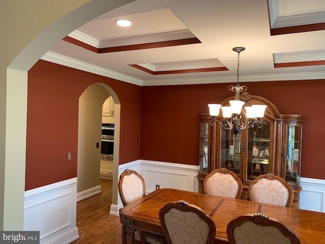 dining area featuring wood-type flooring, a tray ceiling, an inviting chandelier, and ornamental molding