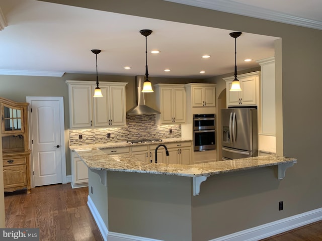 kitchen with decorative light fixtures, stainless steel appliances, light stone counters, and wall chimney range hood