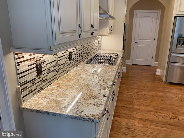 kitchen with tasteful backsplash, light stone counters, stainless steel appliances, extractor fan, and light hardwood / wood-style flooring