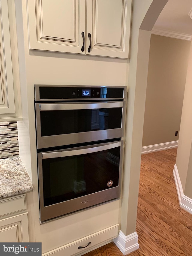 room details featuring light stone countertops, backsplash, ornamental molding, double oven, and light hardwood / wood-style flooring