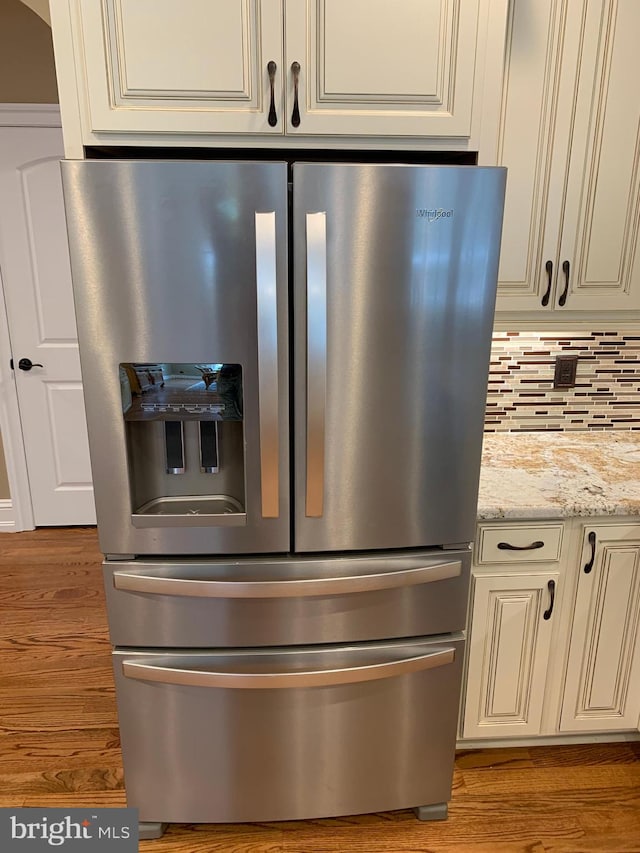 interior details with light stone countertops, stainless steel refrigerator with ice dispenser, backsplash, and hardwood / wood-style floors