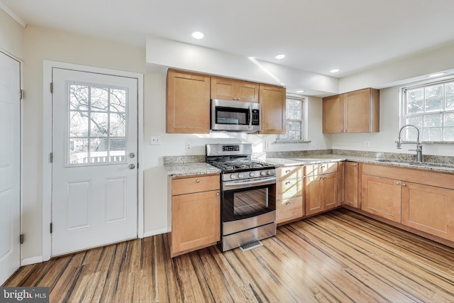 kitchen featuring light stone counters, sink, appliances with stainless steel finishes, and light hardwood / wood-style flooring