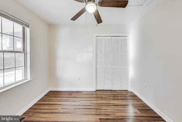 unfurnished bedroom with ceiling fan, a closet, dark wood-type flooring, and multiple windows