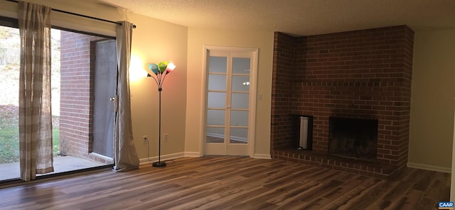 unfurnished living room featuring dark hardwood / wood-style flooring, a textured ceiling, and a brick fireplace