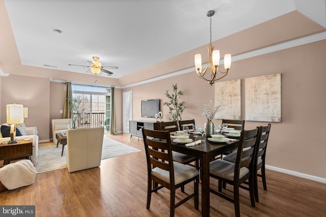 dining space featuring a raised ceiling, crown molding, ceiling fan with notable chandelier, and hardwood / wood-style floors