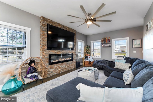 living room featuring dark hardwood / wood-style floors, a stone fireplace, and ceiling fan