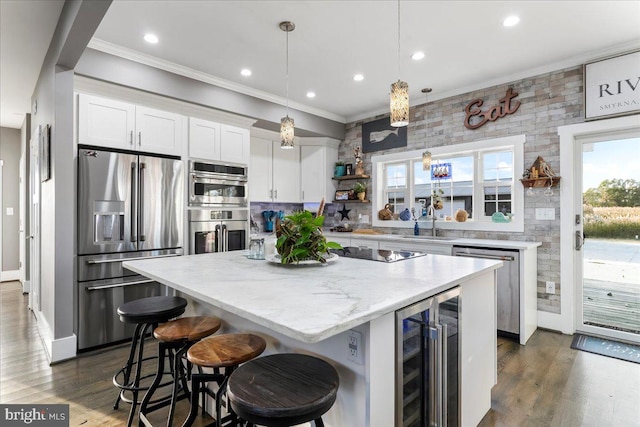 kitchen featuring a center island, beverage cooler, decorative light fixtures, white cabinets, and appliances with stainless steel finishes