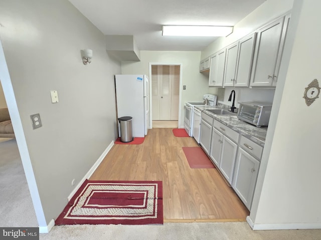 kitchen featuring light stone counters, sink, white appliances, and light wood-type flooring