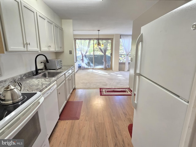 kitchen featuring white appliances, light colored carpet, sink, pendant lighting, and white cabinets