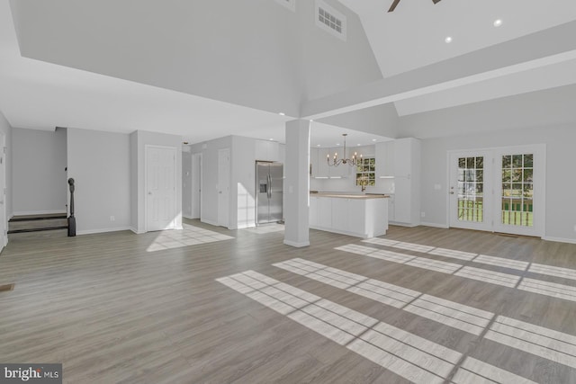 unfurnished living room with ceiling fan with notable chandelier, light wood-type flooring, and high vaulted ceiling