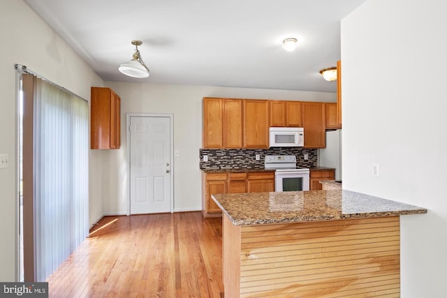 kitchen with kitchen peninsula, dark stone countertops, pendant lighting, white appliances, and light wood-type flooring