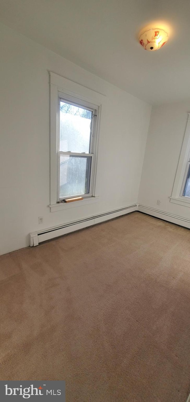 carpeted empty room featuring a baseboard heating unit