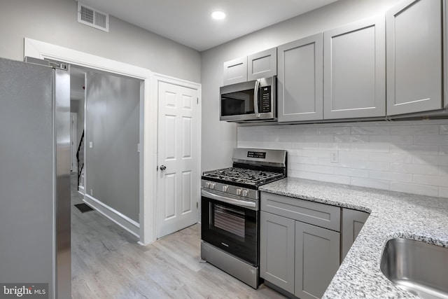 kitchen with gray cabinets, stainless steel appliances, and light wood-type flooring