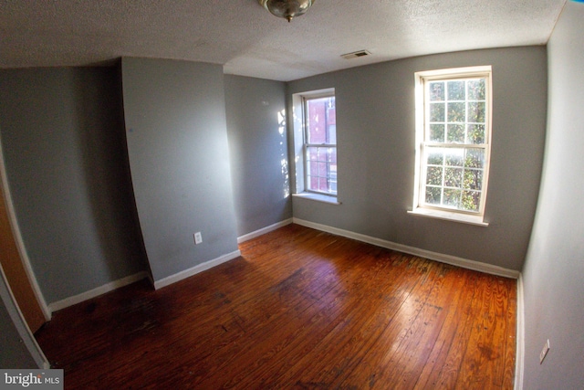 spare room featuring a textured ceiling, dark hardwood / wood-style flooring, and a healthy amount of sunlight