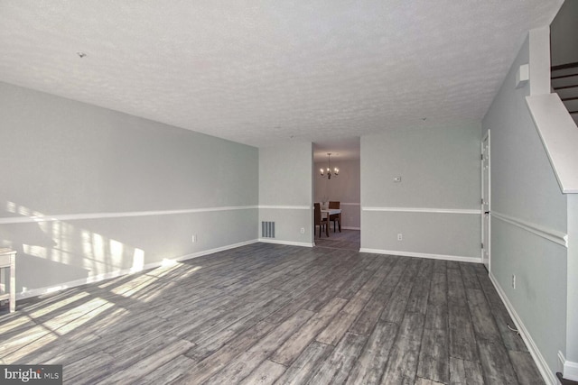 unfurnished living room featuring a chandelier, a textured ceiling, and dark wood-type flooring