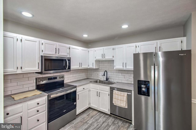 kitchen with appliances with stainless steel finishes, light hardwood / wood-style flooring, white cabinetry, and sink