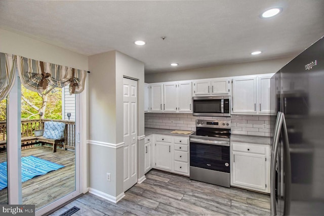 kitchen with white cabinets, light wood-type flooring, stainless steel appliances, and tasteful backsplash