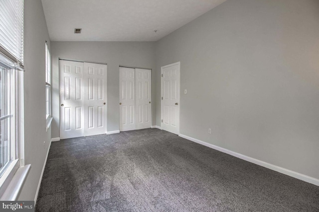 unfurnished bedroom featuring dark carpet, two closets, vaulted ceiling, and multiple windows