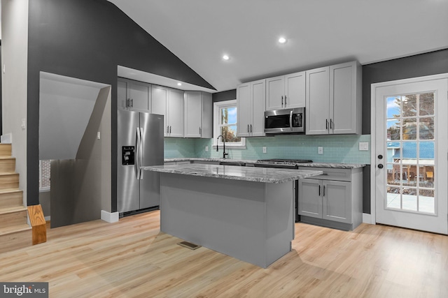 kitchen featuring light stone countertops, gray cabinetry, stainless steel appliances, light hardwood / wood-style floors, and a kitchen island