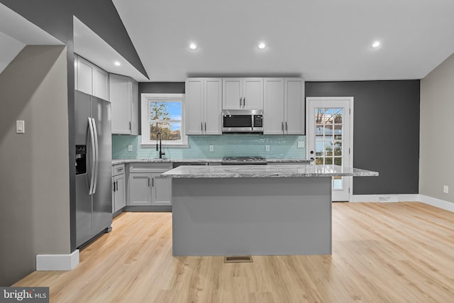 kitchen featuring a center island, stainless steel appliances, light stone counters, and a healthy amount of sunlight