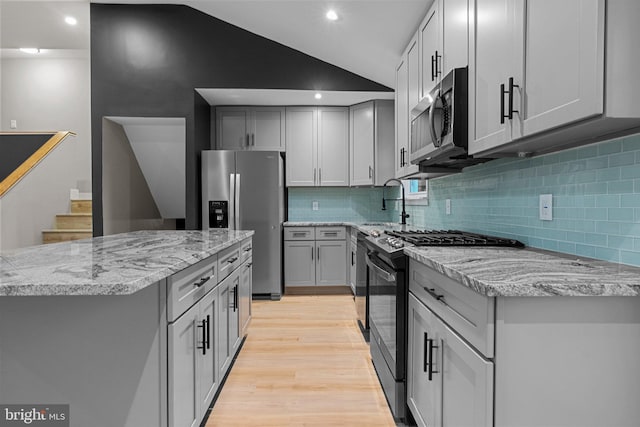 kitchen featuring appliances with stainless steel finishes, tasteful backsplash, light hardwood / wood-style floors, vaulted ceiling, and gray cabinets