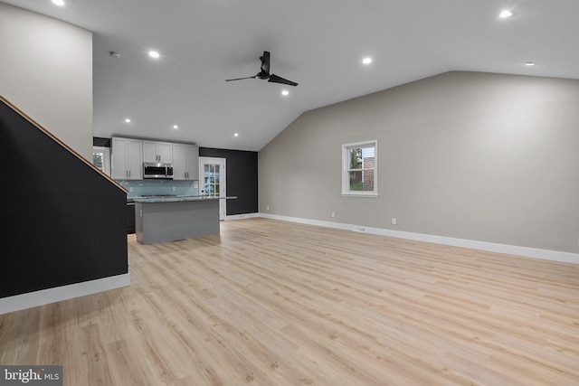 unfurnished living room with ceiling fan, vaulted ceiling, and light wood-type flooring