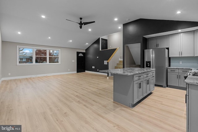 kitchen with light stone countertops, stainless steel refrigerator with ice dispenser, gray cabinets, and lofted ceiling