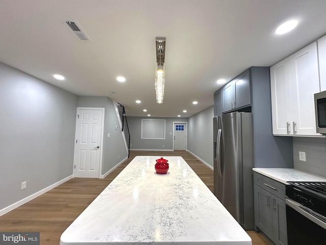 kitchen with appliances with stainless steel finishes, dark hardwood / wood-style flooring, a kitchen island, and light stone counters