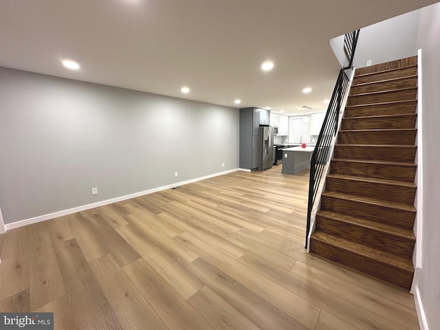 basement with stainless steel fridge and light hardwood / wood-style flooring