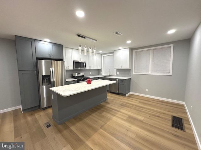 kitchen with appliances with stainless steel finishes, light hardwood / wood-style flooring, hanging light fixtures, and sink