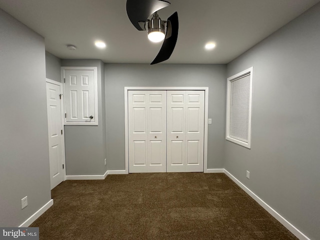 unfurnished bedroom with dark colored carpet, a closet, and ceiling fan