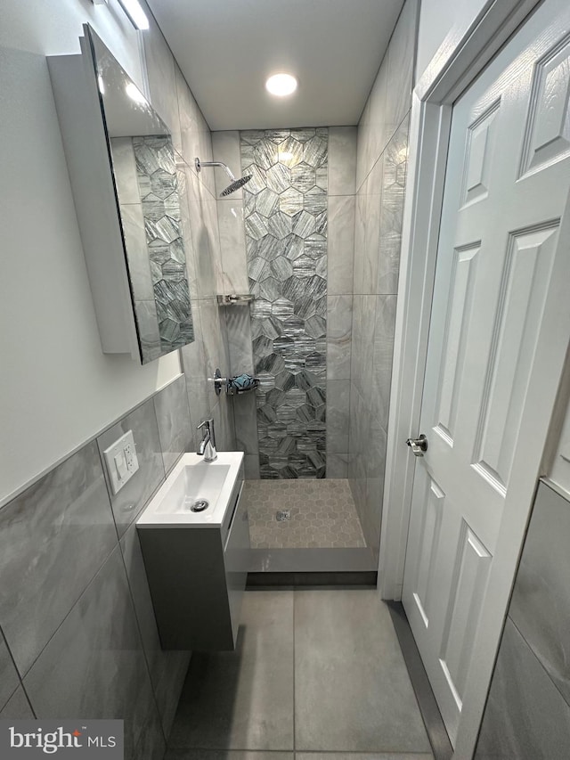 bathroom featuring a tile shower, vanity, and tile walls