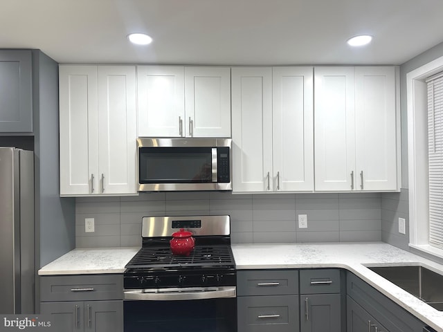 kitchen featuring gray cabinetry, decorative backsplash, light stone counters, and stainless steel appliances