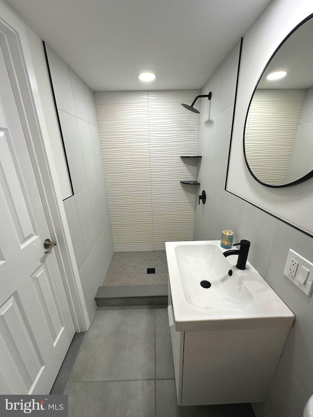 bathroom featuring tile patterned floors, vanity, a tile shower, and tile walls