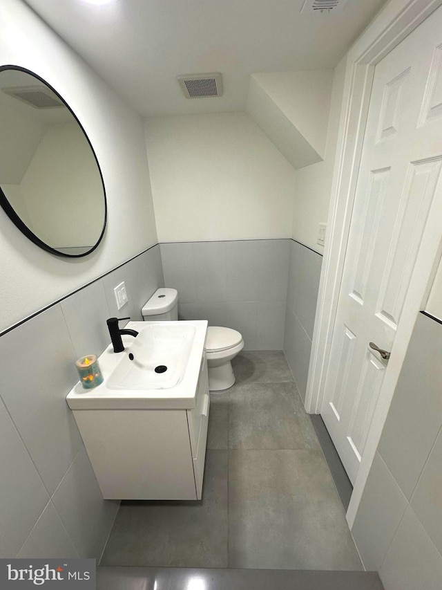 bathroom with vanity, toilet, and tile walls