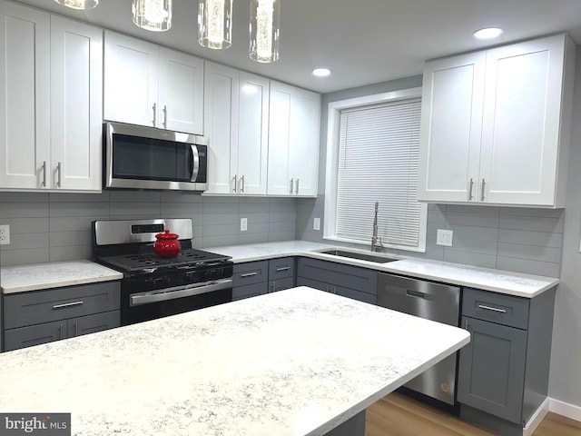 kitchen featuring hanging light fixtures, sink, light hardwood / wood-style flooring, decorative backsplash, and appliances with stainless steel finishes