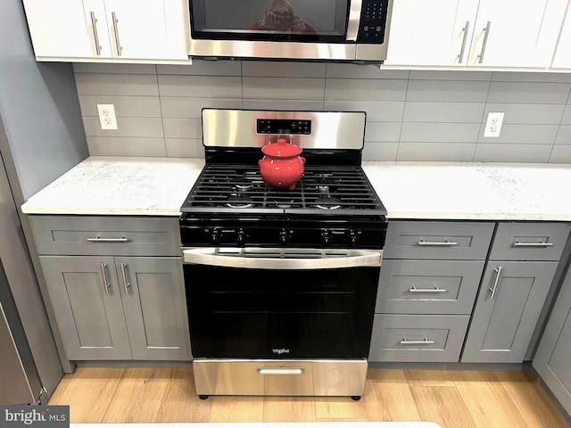 kitchen with backsplash, gray cabinets, light hardwood / wood-style flooring, and stainless steel appliances