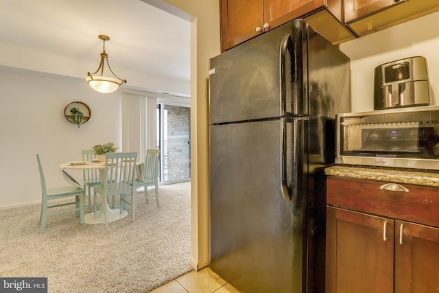 kitchen featuring light stone counters, black refrigerator, light tile patterned floors, and pendant lighting